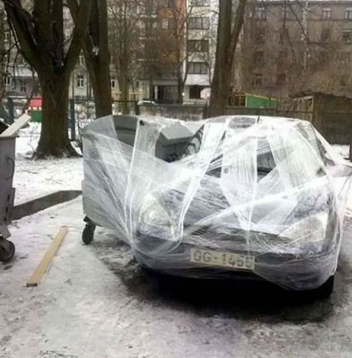 An example of outrageous parking, a car completely wrapped in plastic on a snowy street.