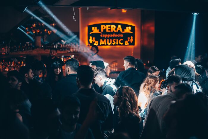 A lively bar scene with a crowd of people and bright lights, showing conversations overheard by bartenders.