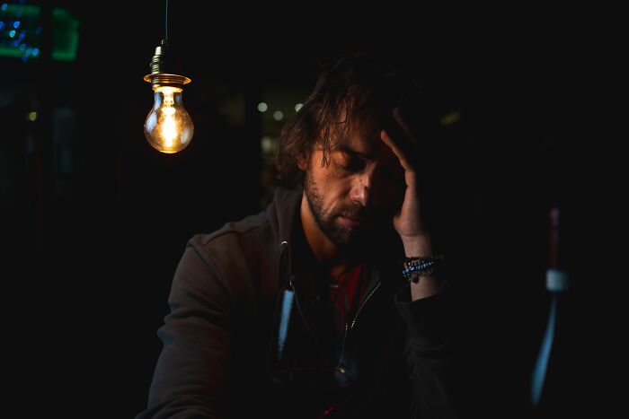A man looking distressed under a single light, representing the emotional impact of conversations bartenders overheard.