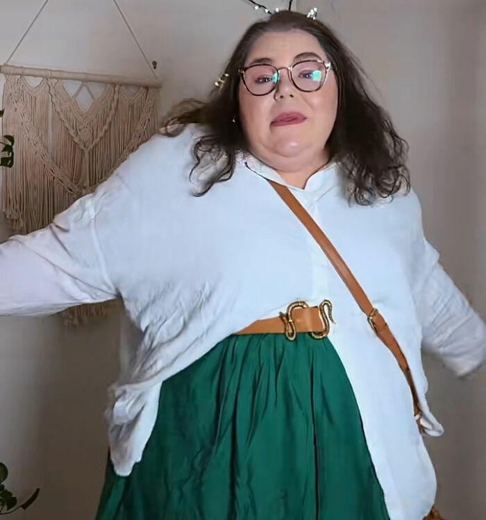 A plus-size influencer in glasses, a white shirt, green skirt, and a brown belt posing for the camera, discussing clothing selection. A plus-size influencer in glasses, a white shirt, green skirt, and a brown belt posing for the camera, discussing clothing selection.