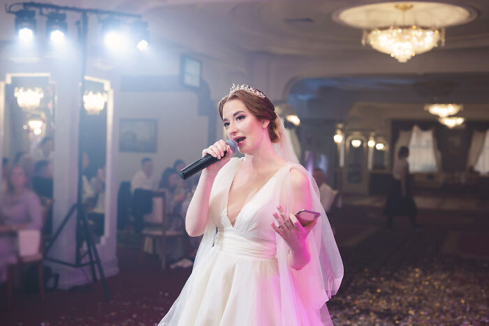 A bride singing into a microphone at her wedding reception, regretting time and money on this wedding.