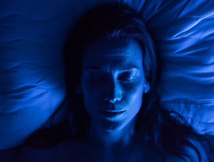 A woman with blue light on her face, sleeping peacefully in bed. Beautiful facts about sleep.