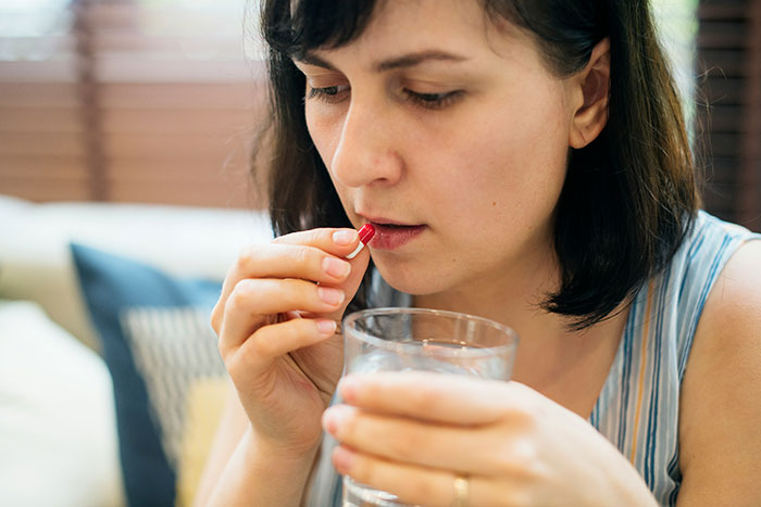 A woman taking a pill with a glass of water, highlighting beautiful facts about health.