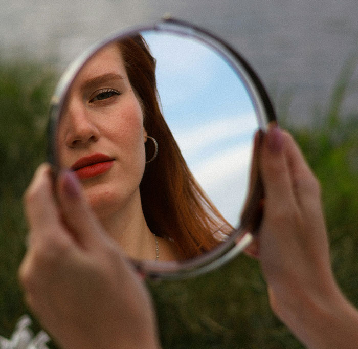 A woman holding a mirror reflecting her face and the sky, showcasing beautiful facts that are real.
