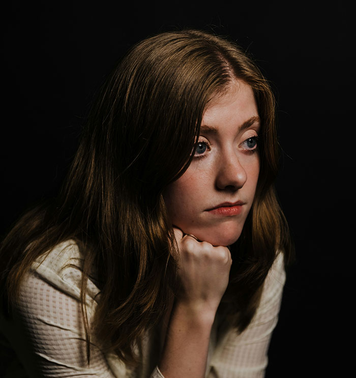 A thoughtful young woman with brown hair and blue eyes, looking away. Discover beautiful facts that are real.
