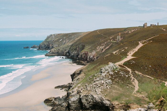 Dramatic coastal cliffs and a sandy beach, with an old mine building on the hill, evoking extraordinary stories from World War II.