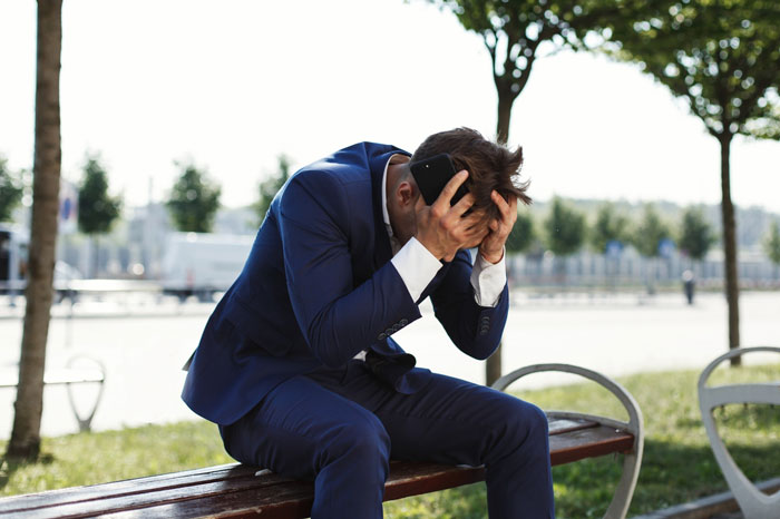 A man in a suit looks distraught while holding his head, representing the betrayal of trust and business. A man in a suit looks distraught while holding his head, representing the betrayal of trust and business.