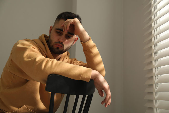 A man with a beard in a yellow hoodie sits with his hand on his head, looking sad, reflecting on a friend copying his business. A man with a beard in a yellow hoodie sits with his hand on his head, looking sad, reflecting on a friend copying his business.