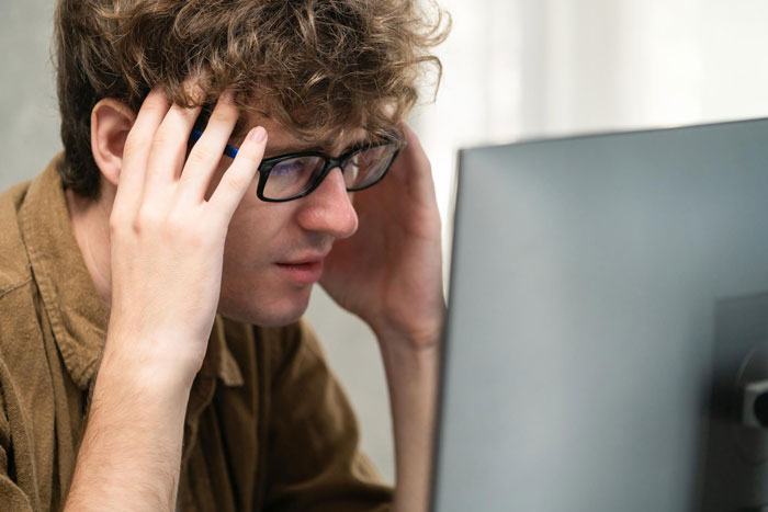 A man with curly hair and glasses looking stressed at a computer, symbolizing the impact of a copied business. A man with curly hair and glasses looking stressed at a computer, symbolizing the impact of a copied business.