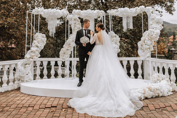A happy groom and bride at their wedding, with white floral arches in the background, unaware of the friend's withdrawal issues. A happy groom and bride at their wedding, with white floral arches in the background, unaware of the friend's withdrawal issues.