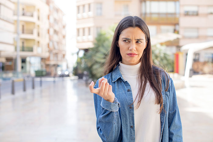A woman with long dark hair and a denim jacket, making a gesture of frustration or dismissal, relating to a bride and bridesmaid drama. A woman with long dark hair and a denim jacket, making a gesture of frustration or dismissal, relating to a bride and bridesmaid drama.