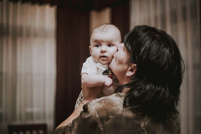 A mother holding and kissing a baby, a moment of peace despite the worst MILs.