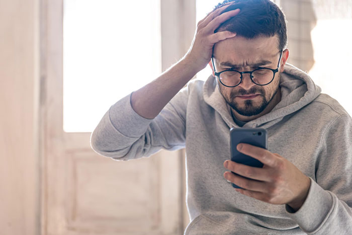 A guy looking confused while holding a phone, reacting to his GF's claim of not speaking for 10 years.