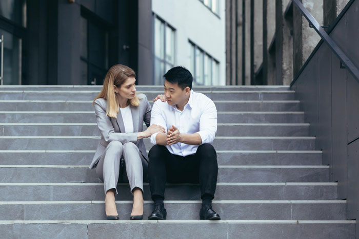 A man and woman sitting on stairs, the woman comforting the man, both discussing the GF's claims.