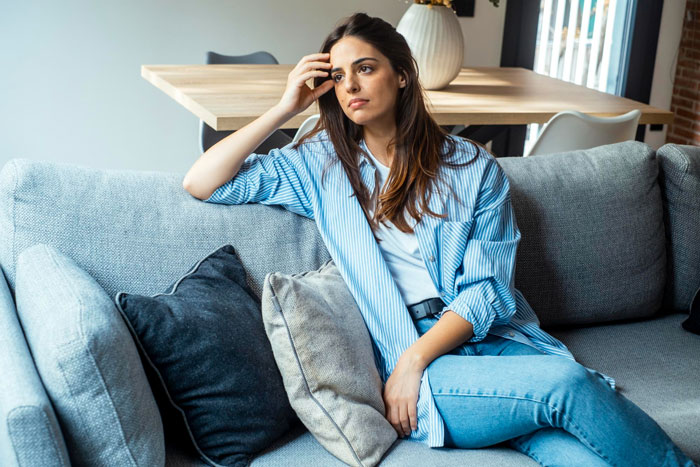 Woman sitting on a couch, looking confused about her guy knowing every detail despite 10 years of no contact.