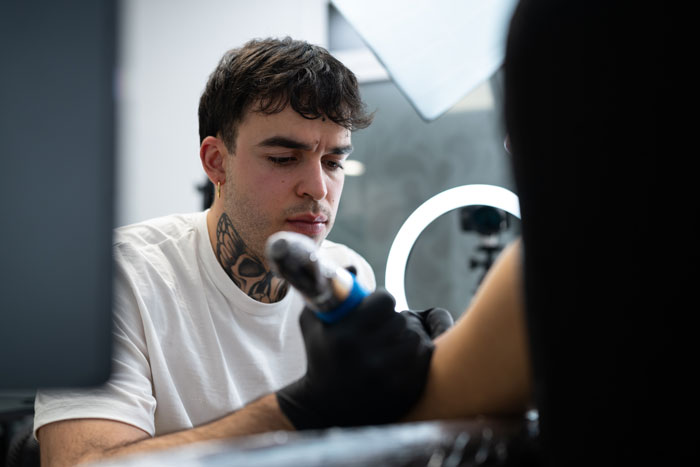 A tattoo artist focusing intently while giving a tattoo, a requested tattoo in the industry.