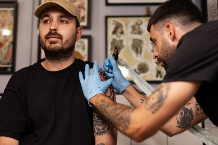 A tattoo artist in blue gloves giving a forearm tattoo to a client, a requested tattoo in the industry.