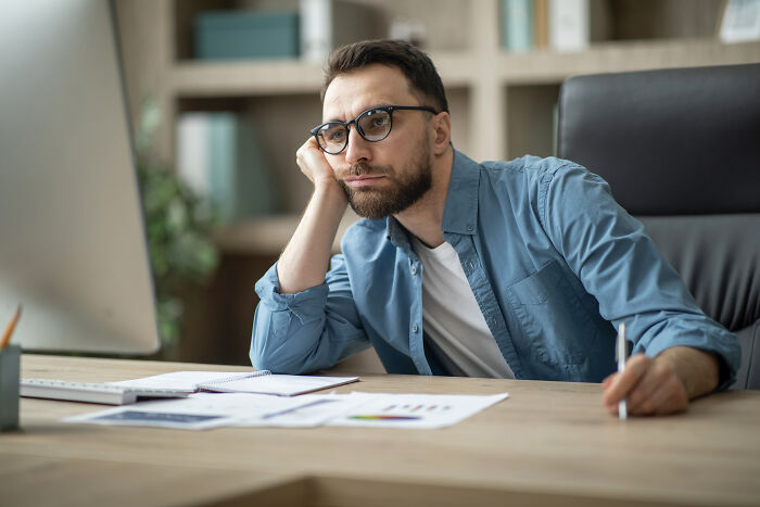 A tired worker looks bored at a computer, reflecting the feeling of corporate buzzwords.