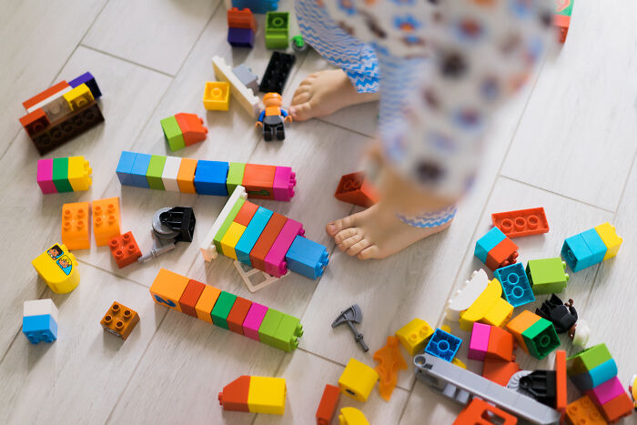 A child's bare feet among scattered colorful building blocks, symbolizing messy guests who ignored house etiquette.