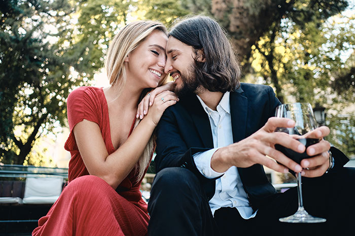 A happy young couple smiling and embracing, enjoying a glass of red wine outdoors, illustrating a guy pretending to be younger. A happy young couple smiling and embracing, enjoying a glass of red wine outdoors, illustrating a guy pretending to be younger.