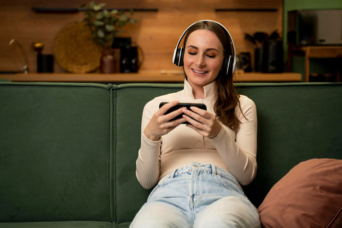 A woman wearing headphones smiles while looking at her phone app, explaining why her boyfriend deleting it hurt. A woman wearing headphones smiles while looking at her phone app, explaining why her boyfriend deleting it hurt.