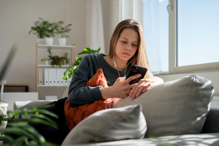 A thoughtful woman on a couch with headphones, looking at her phone, reflecting on her boyfriend deleting her app. A thoughtful woman on a couch with headphones, looking at her phone, reflecting on her boyfriend deleting her app.