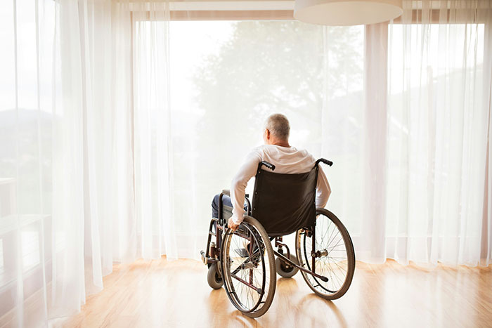 A man in a wheelchair looking out a large window, symbolizing the groom's friend who is in a wheelchair and causes the bride to question her future.