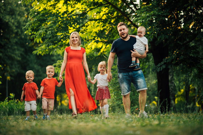 A family with a SAHM wife, four young children, and a father holding a baby, happy in a park setting. A family with a SAHM wife, four young children, and a father holding a baby, happy in a park setting.