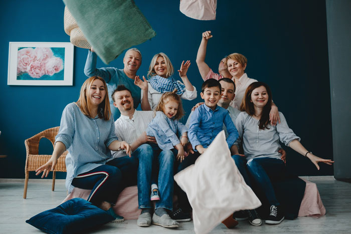 A large family, including a guy, his wife, and children, smiling while throwing pillows, highlighting family life. A large family, including a guy, his wife, and children, smiling while throwing pillows, highlighting family life.