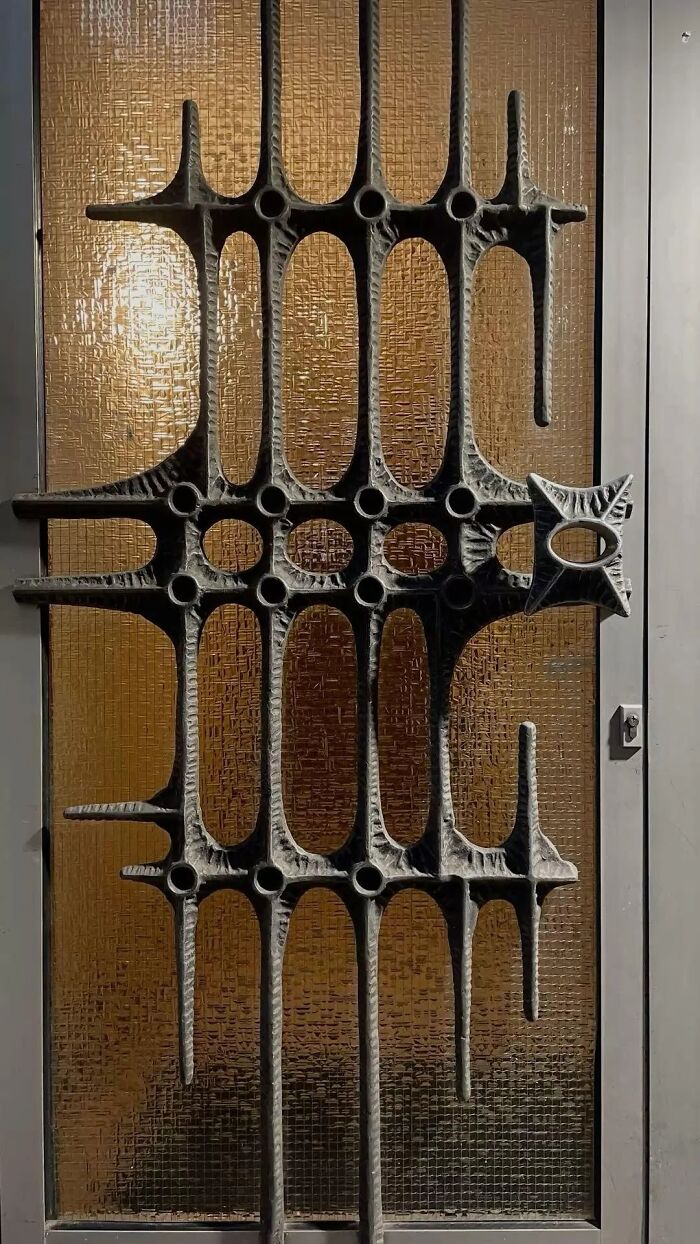 Close-up of a remarkable design featuring an abstract, sculptural metal door grill against patterned glass, highlighting historic interiors.