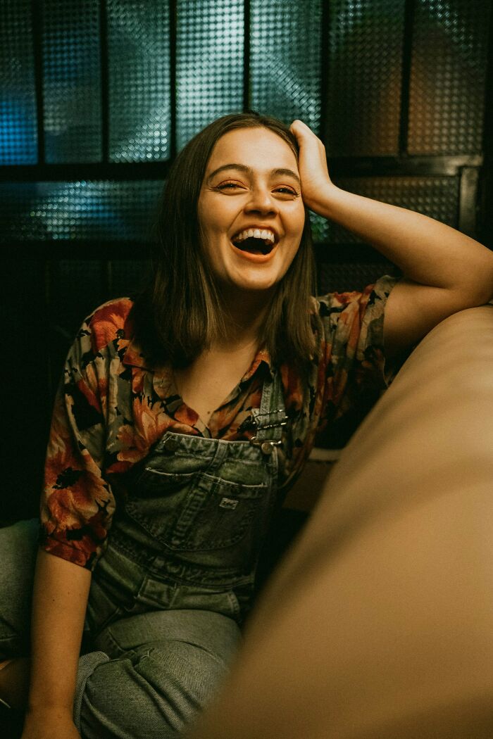 A young woman with a floral shirt and overalls laughs heartily, showing the joy of micro feminism.