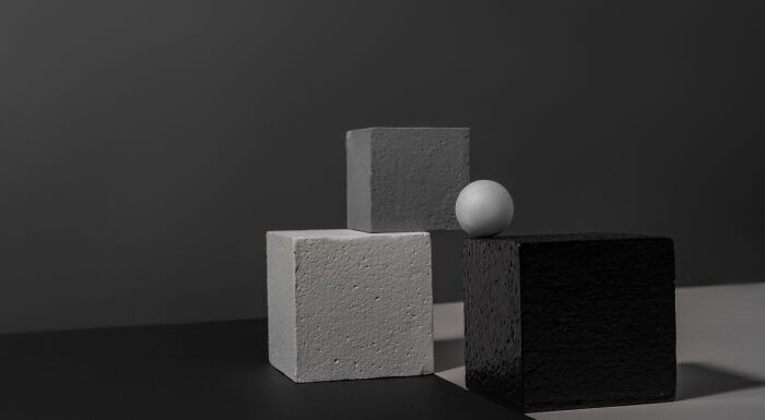 A minimalistic image with three cubes in different shades of gray and a white sphere, symbolizing philosophy and knowledge.