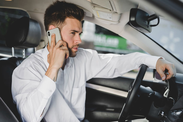 A man in a white shirt with a beard and short hair talking on a phone while sitting in a car, an annoying driver in a parking war.