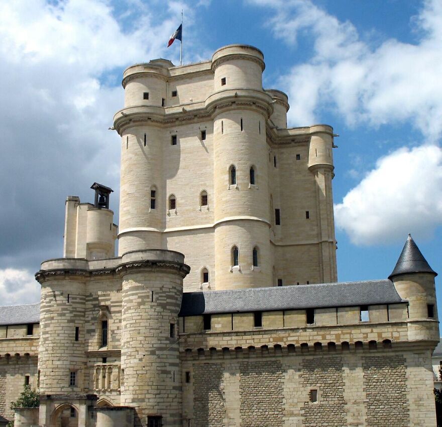 Beautiful castles, a grand castle with multiple towers and a French flag against a cloudy sky.