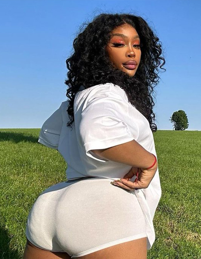 SZA, a celebrity BBL disaster example, outdoors in a field, wearing a white shirt and shorts.