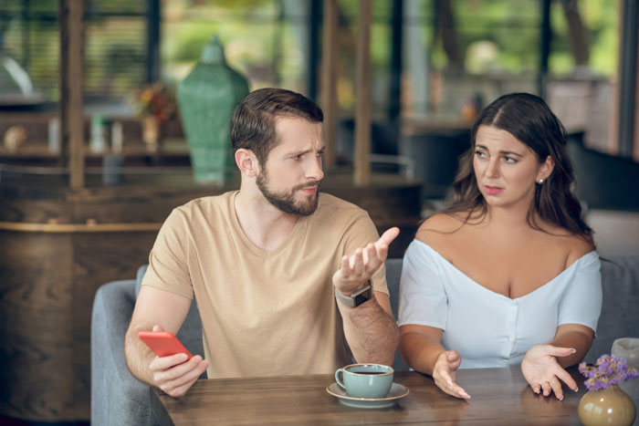 A man and woman in a cafe, looking surprised and discussing relationship issues with a cheating girlfriend.