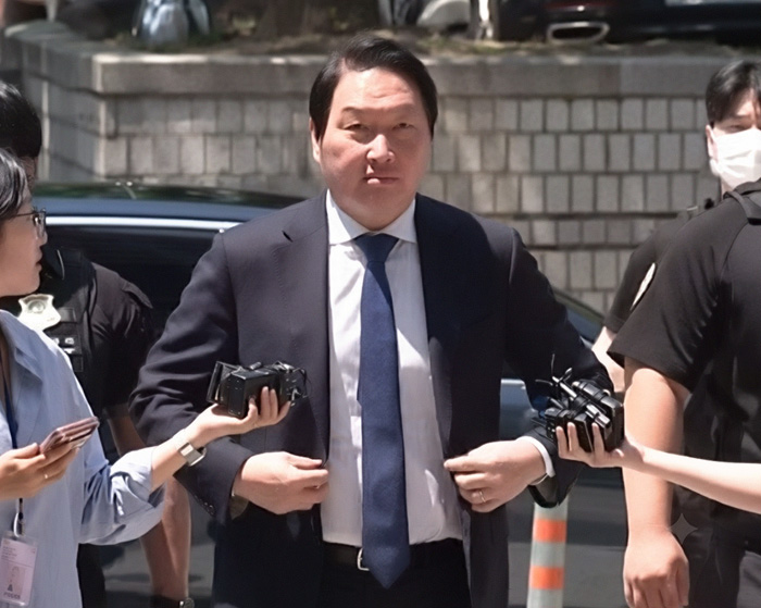 A billionaire man in a suit, at the center of a high-profile divorce case, surrounded by reporters. A billionaire man in a suit, at the center of a high-profile divorce case, surrounded by reporters.