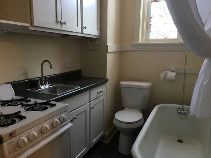 A terribly designed bathroom with a stove, sink, toilet, and bathtub all in a tiny space.