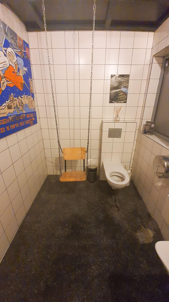 A bizarrely designed bathroom with a swing hanging next to the toilet, inside a tiled room.