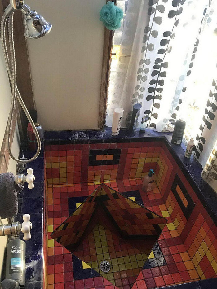 A terribly designed bathroom with a small, colorful tiled shower and bathtub that has a pyramid-like structure in the middle.
