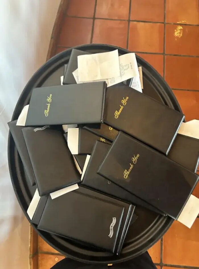 Service industry workers handle a tray full of bill folders and receipts, indicating a busy shift.