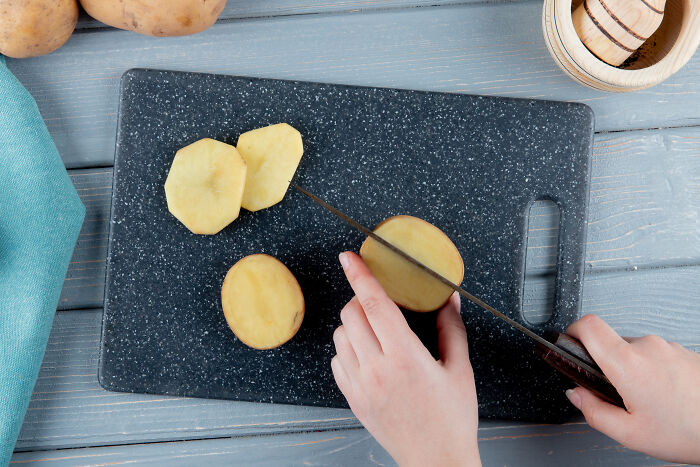 Hands slicing potatoes on a dark cutting board, illustrating one of the industries that actually make millions.
