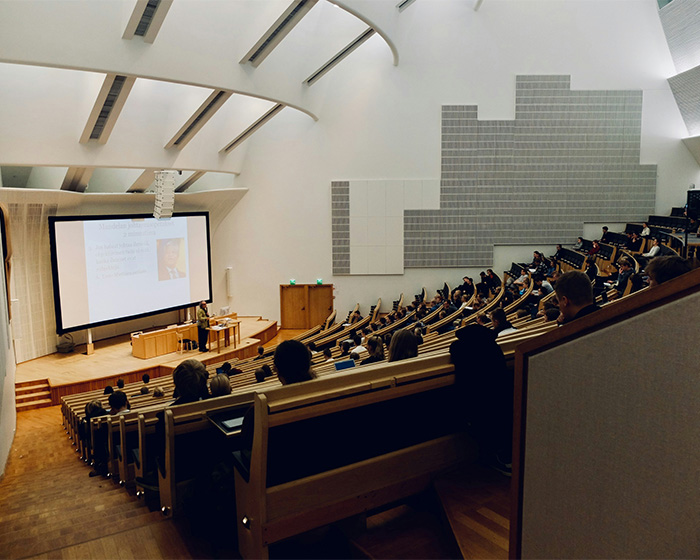 A college professor lecturing a large class, using a clever trick to catch students using AI on their final.