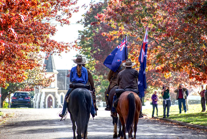 Two riders on horseback, carrying flags, on a tree-lined road in autumn, symbolizing countries surviving nuclear war.