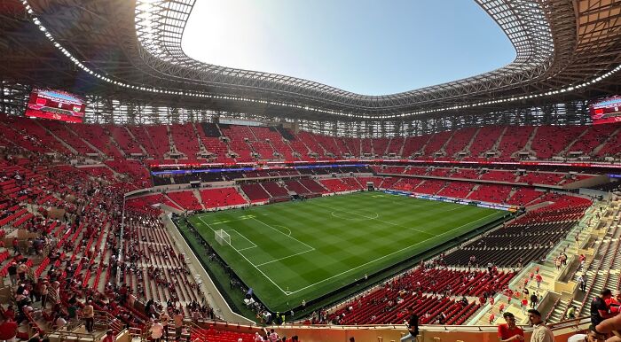 A sprawling FIFA World Cup stadium with a vibrant green pitch surrounded by countless red seats, many filled with fans. A sprawling FIFA World Cup stadium with a vibrant green pitch surrounded by countless red seats, many filled with fans.
