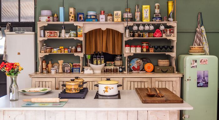 A vintage kitchen with a white wooden hutch filled with various jars, cans, and mugs, reflecting home economics.