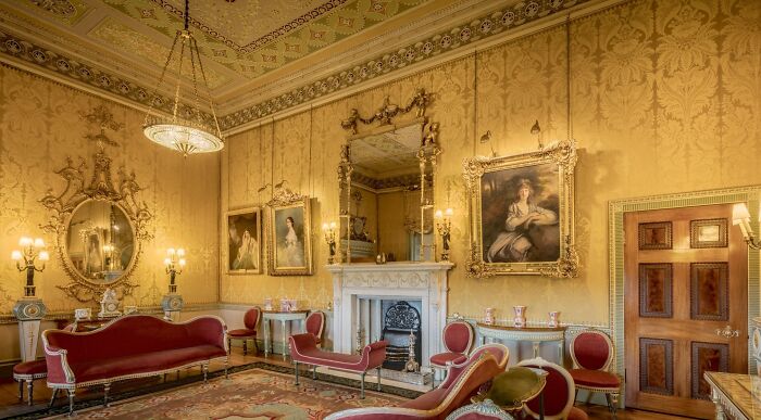 A grand Regency world room with ornate gold wallpaper, framed paintings, red velvet furniture, and sparkling chandeliers, perfect for Bridgerton fans. A grand Regency world room with ornate gold wallpaper, framed paintings, red velvet furniture, and sparkling chandeliers, perfect for Bridgerton fans.