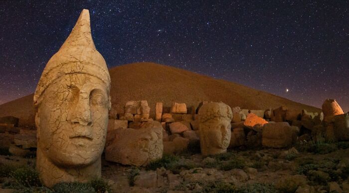 Massive stone heads from ancient civilizations stand against a starry night sky, hinting at lost cities and historical mysteries.