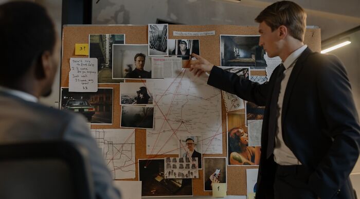 Two sharp thinkers, possibly FBI agents, examining a cork board filled with photos, maps, and notes for a challenge. Two sharp thinkers, possibly FBI agents, examining a cork board filled with photos, maps, and notes for a challenge.