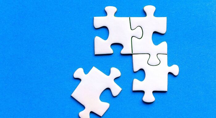 Several white puzzle pieces on a blue background, some connected, one separate, representing pop culture rebus puzzles. Several white puzzle pieces on a blue background, some connected, one separate, representing pop culture rebus puzzles.